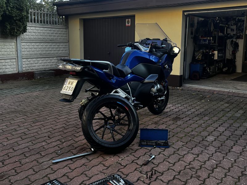 Motocykl BMW przed garażem ze zdjętym tylnym kołem, na kostce rozłożone zestawy kluczy