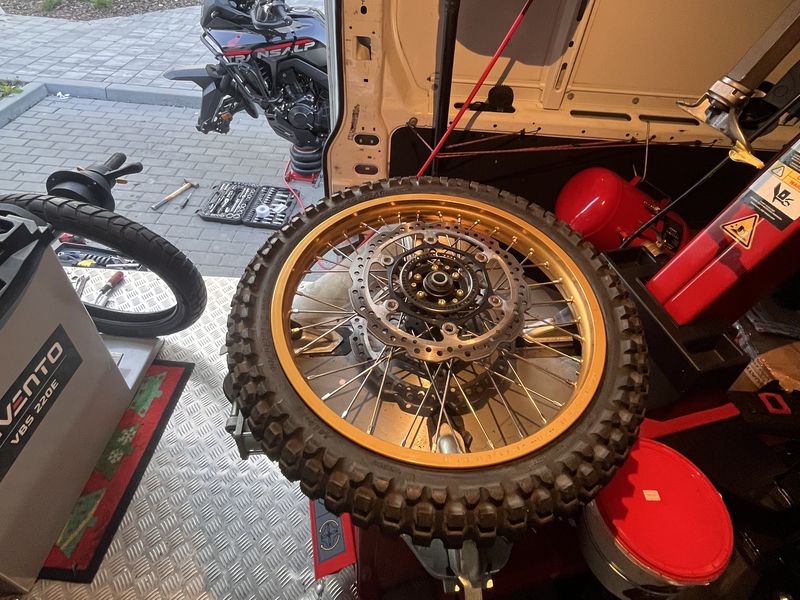 Koło motocykla enduro oparte o otwarte drzwi busa na miejskim chodniku