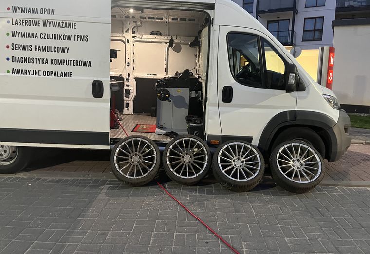 Otwarty bus serwisowy z montażownicą w środku, przed nim cztery koła z felgami aluminiowymi